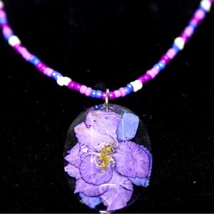 A purple seed bead necklace with a resin flower pendant